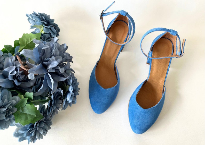 May include: A pair of blue suede heeled shoes with ankle straps. The shoes have a pointed toe and a block heel.