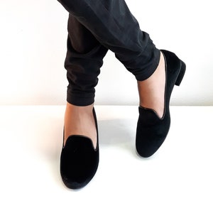 K&ouml;nnte beinhalten: Ein Paar schwarze Samt-Slipper mit dezentem Glanz. Die Slipper haben ein schlichtes Design und eine abgerundete Spitze.