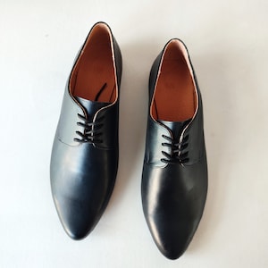 Puede incluir: Un par de zapatos negros de cuero con cordones y punta puntiaguda.