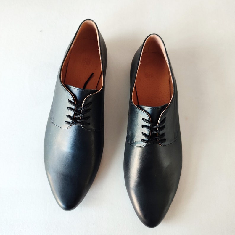 Puede incluir: Un par de zapatos negros de cuero con cordones y punta puntiaguda.
