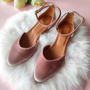 May include: A pair of dusty rose velvet ankle strap flats with a pointed toe.
