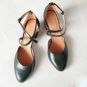 May include: A pair of dark green leather heeled shoes with ankle straps and a crisscross design. The shoes have a pointed toe and a small heel. The interior is a light brown color.