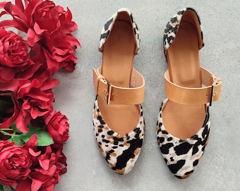 May include: A pair of black and white leopard print shoes with brown leather straps and buckles. The shoes have a pointed toe and a low heel.