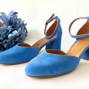 May include: A pair of blue suede heeled shoes with ankle straps. The shoes have a pointed toe and a block heel.