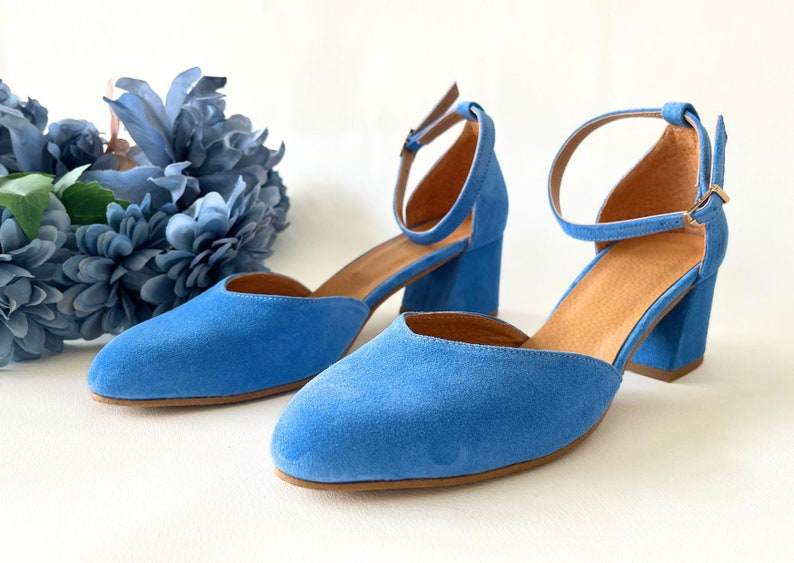 May include: A pair of blue suede heeled shoes with ankle straps. The shoes have a pointed toe and a block heel.
