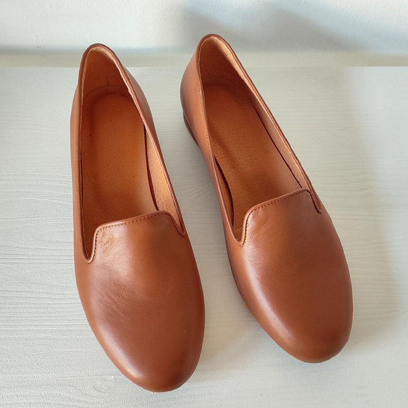 Puede incluir: Un par de mocasines de cuero marr&oacute;n. Los zapatos tienen una punta redondeada y un tac&oacute;n bajo. El cuero tiene una textura suave y un color marr&oacute;n rojizo c&aacute;lido. Los zapatos est&aacute;n dise&ntilde;ados para la comodidad y el estilo.