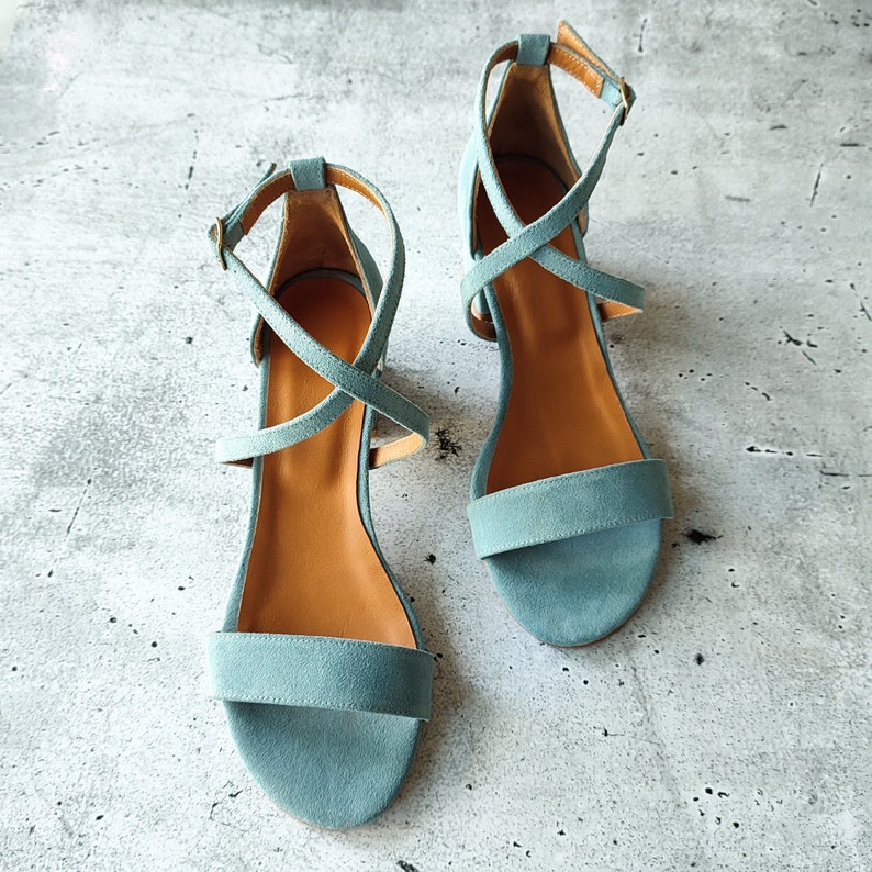 May include: A pair of light blue suede sandals with criss-cross straps and a low heel.
