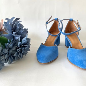 May include: A pair of blue suede heeled shoes with ankle straps. The shoes have a rounded toe and a block heel.