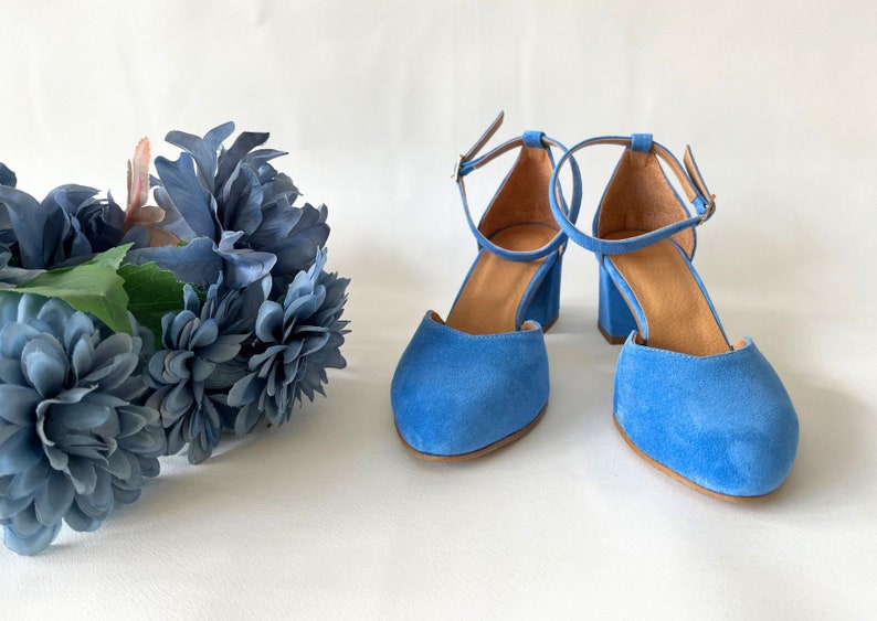 May include: A pair of blue suede heeled shoes with ankle straps. The shoes have a rounded toe and a block heel.