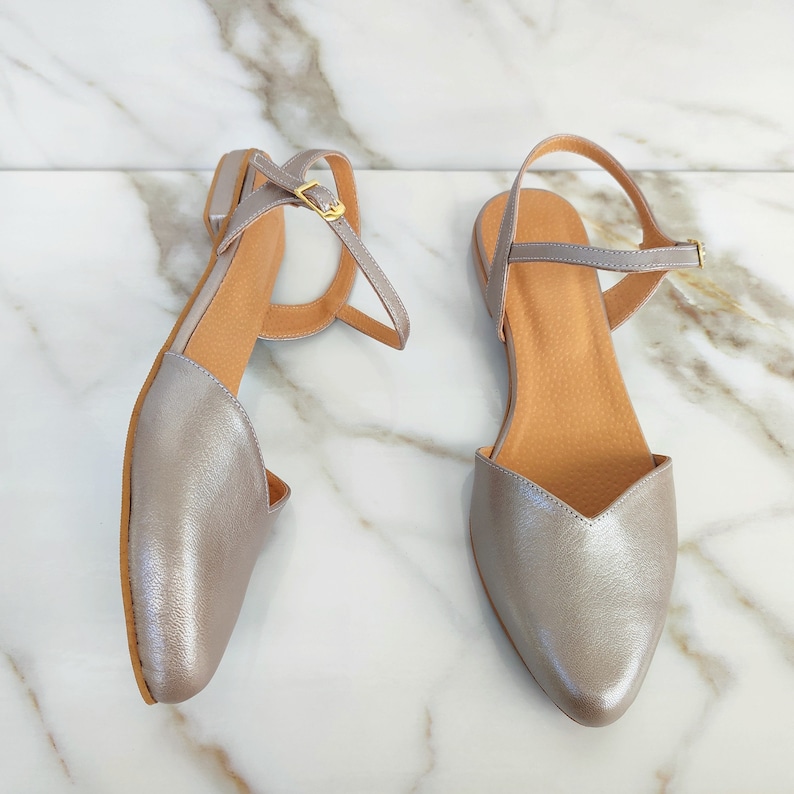 Op de afbeelding: Een paar zilveren metallic sandalen met spitse neus en enkelbandjes. De sandalen hebben een eenvoudig ontwerp en zijn gemaakt van zacht, soepel leer.