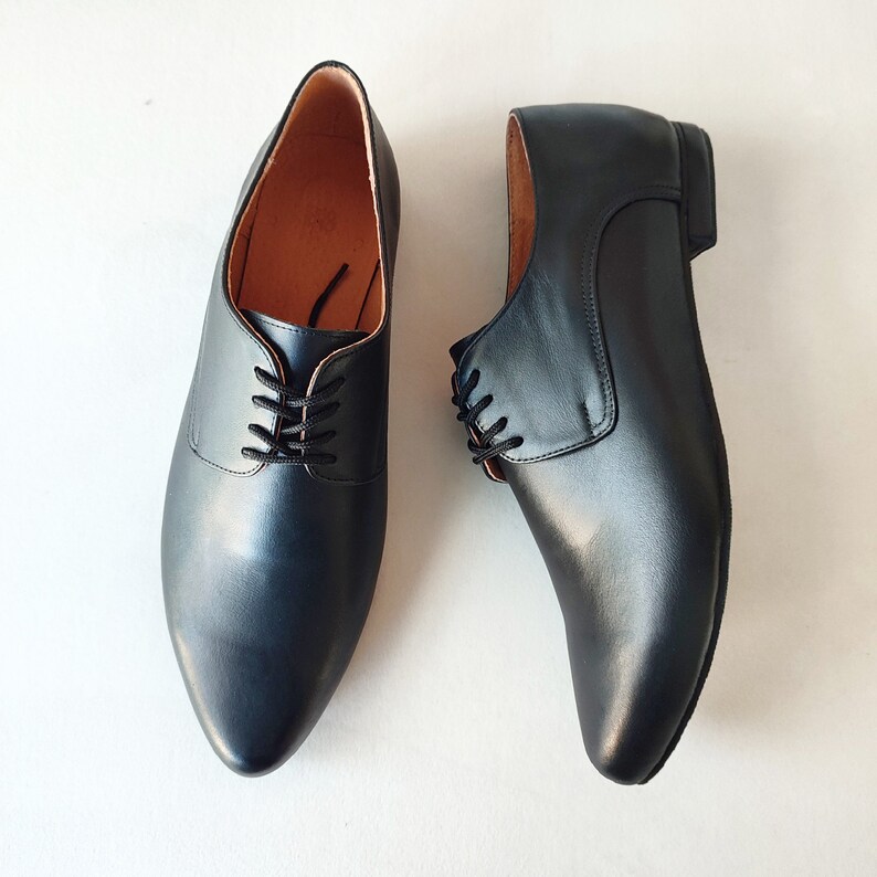 Puede incluir: Un par de zapatos negros de cuero con cordones y punta puntiaguda.