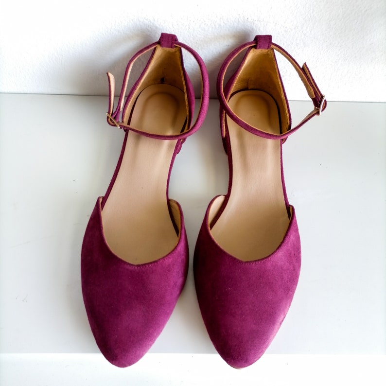 May include: A pair of burgundy suede ankle strap flats with pointed toes.