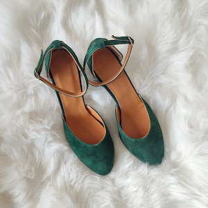 K&ouml;nnte beinhalten: Ein Paar dunkelgr&uuml;ne Wildlederschuhe mit Kn&ouml;chelriemen. Die Schuhe haben eine spitze Zehenpartie und einen niedrigen Absatz.