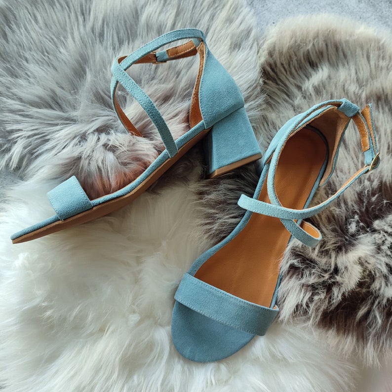 May include: Two pairs of light blue suede heeled sandals with ankle straps. The sandals have a criss-cross strap design and a block heel.