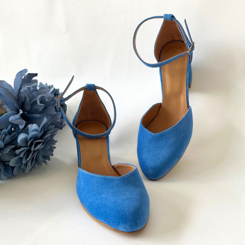 May include: A pair of blue suede heeled shoes with ankle straps. The shoes have a pointed toe and a low block heel.