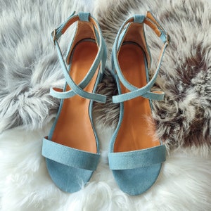 May include: A pair of light blue suede sandals with criss-cross straps. The sandals have a closed toe and a low heel.