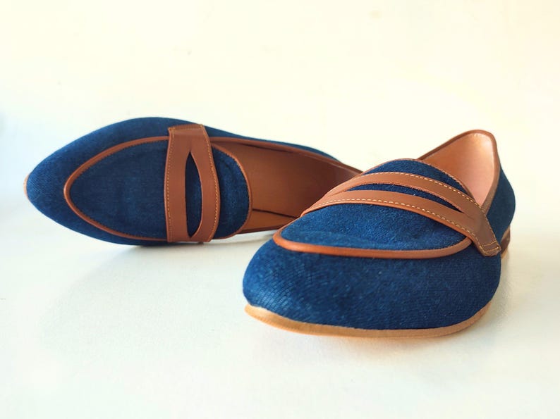 May include: A pair of blue denim loafers with brown leather accents. The loafers have a pointed toe and a low heel.