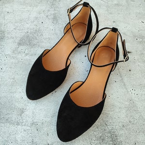 May include: A pair of black suede ankle strap flats with a pointed toe.