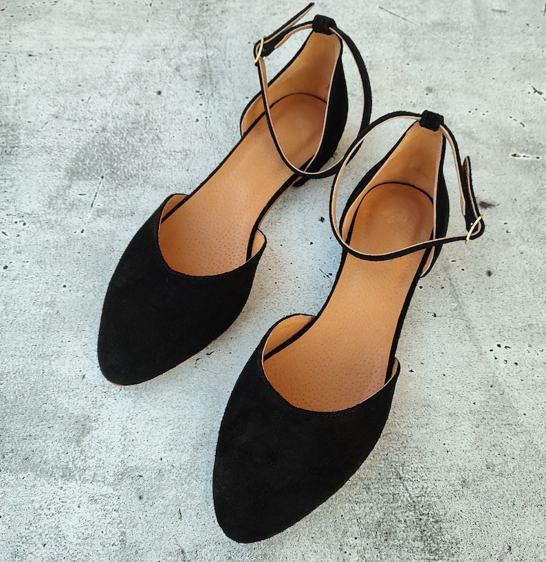 May include: A pair of black suede ankle strap flats with a pointed toe.