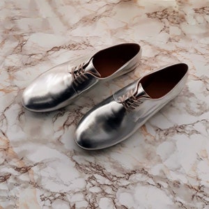 May include: A pair of silver leather shoes with laces. The shoes have a pointed toe and a low heel.