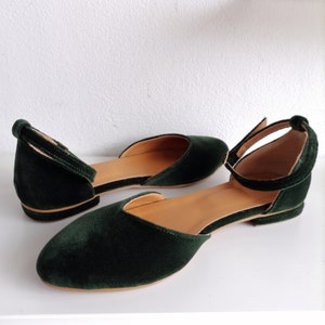 May include: A pair of dark green velvet flats with ankle straps. The shoes have a pointed toe and a low heel.