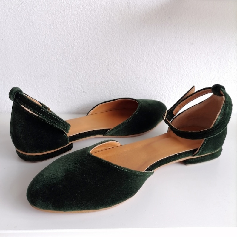 May include: A pair of dark green velvet flats with ankle straps. The shoes have a pointed toe and a low heel.