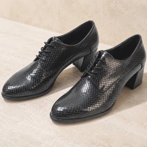 May include: A pair of black, textured leather oxfords with a snakeskin pattern. The shoes have a lace-up design and a block heel. The shoes are displayed on a neutral-colored surface.
