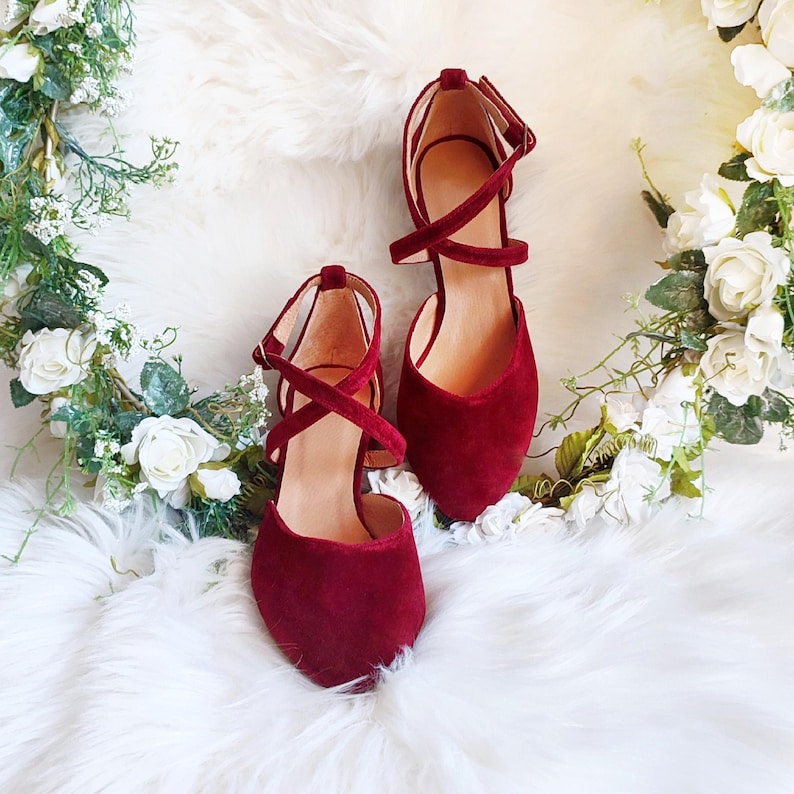 May include: A pair of burgundy suede heeled shoes with criss-cross straps.