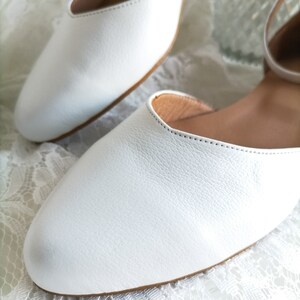 May include: A pair of white leather flats with a simple design. The shoes have a pointed toe and a low heel. The shoes are made of soft, supple leather and have a comfortable fit.