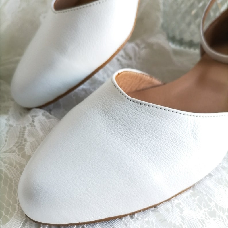 May include: A pair of white leather flats with a simple design. The shoes have a pointed toe and a low heel. The shoes are made of soft, supple leather and have a comfortable fit.