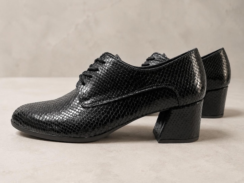 May include: Black, textured leather oxfords with a low, block heel. The shoes have a lace-up closure and a rounded toe. The leather has a snakeskin pattern. The shoes are set against a neutral background.