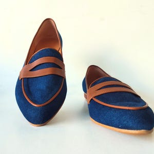 May include: A pair of blue denim loafers with brown leather accents. The loafers have a pointed toe and a low heel.