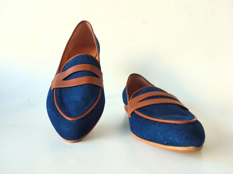 May include: A pair of blue denim loafers with brown leather accents. The loafers have a pointed toe and a low heel.