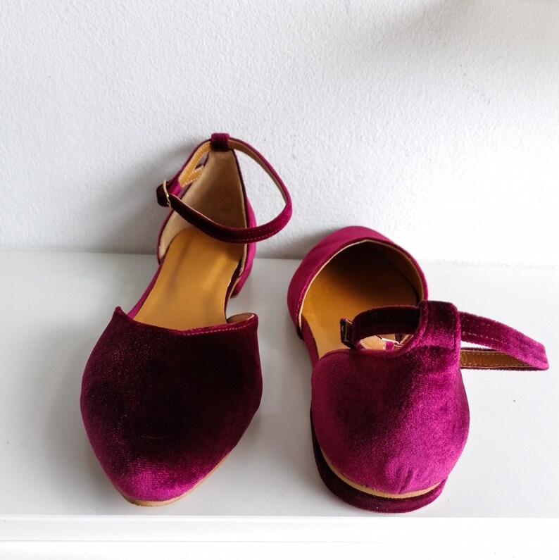 May include: A pair of burgundy velvet ankle strap flats. The shoes have a pointed toe and a low heel.