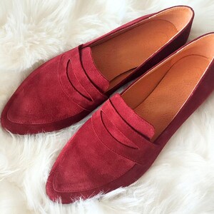 May include: A pair of burgundy suede loafers with a pointed toe and a single strap across the vamp.