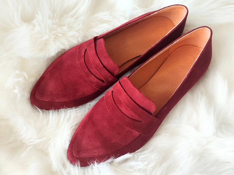 May include: A pair of burgundy suede loafers with a pointed toe and a single strap across the vamp.