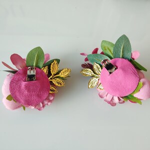 May include: Two pink flower hair clips with gold leaves and green foliage. The back of each clip has a pink felt backing with a metal clip.