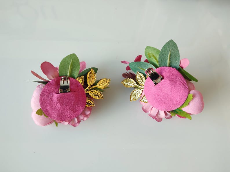 May include: Two pink flower hair clips with gold leaves and green foliage. The back of each clip has a pink felt backing with a metal clip.