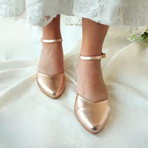 May include: Rose gold ankle strap flat shoes with a pointed toe.