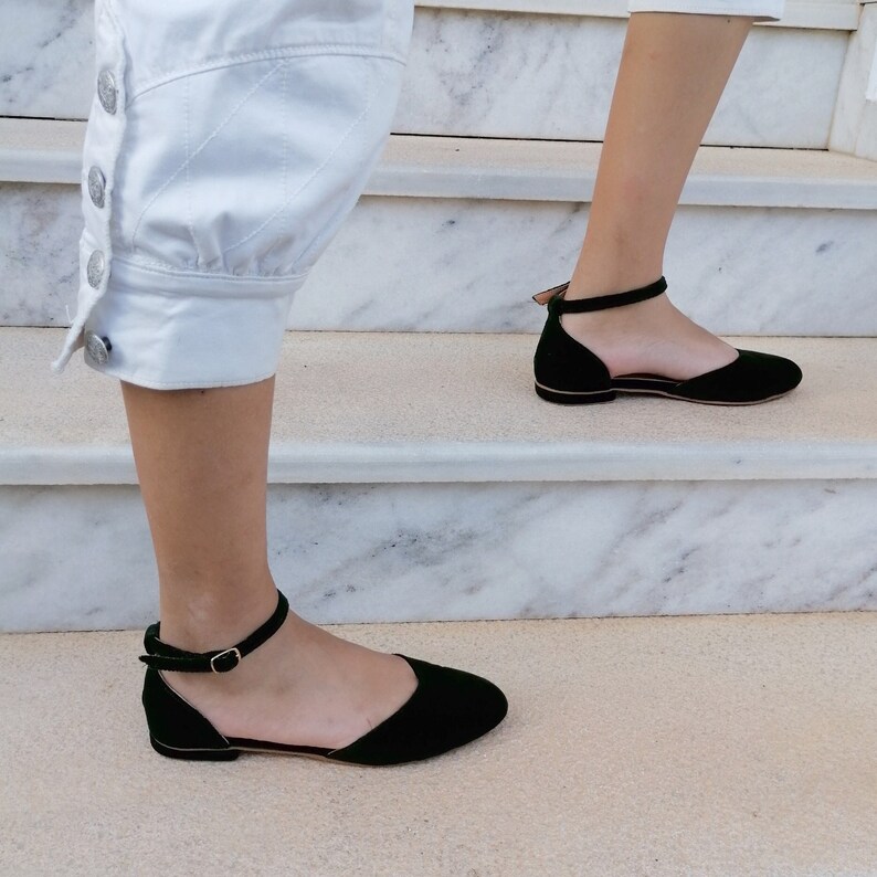 May include: A pair of black ankle strap flats with a pointed toe. The shoes are made of suede and have a low heel.