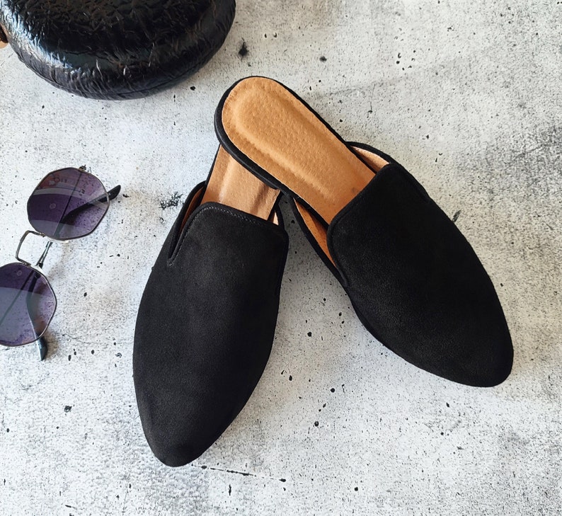 K&ouml;nnte beinhalten: Zwei Paar schwarze Wildlederslipper mit brauner Ledersohle. Die Slipper haben eine spitze Zehenpartie und einen niedrigen Absatz.
