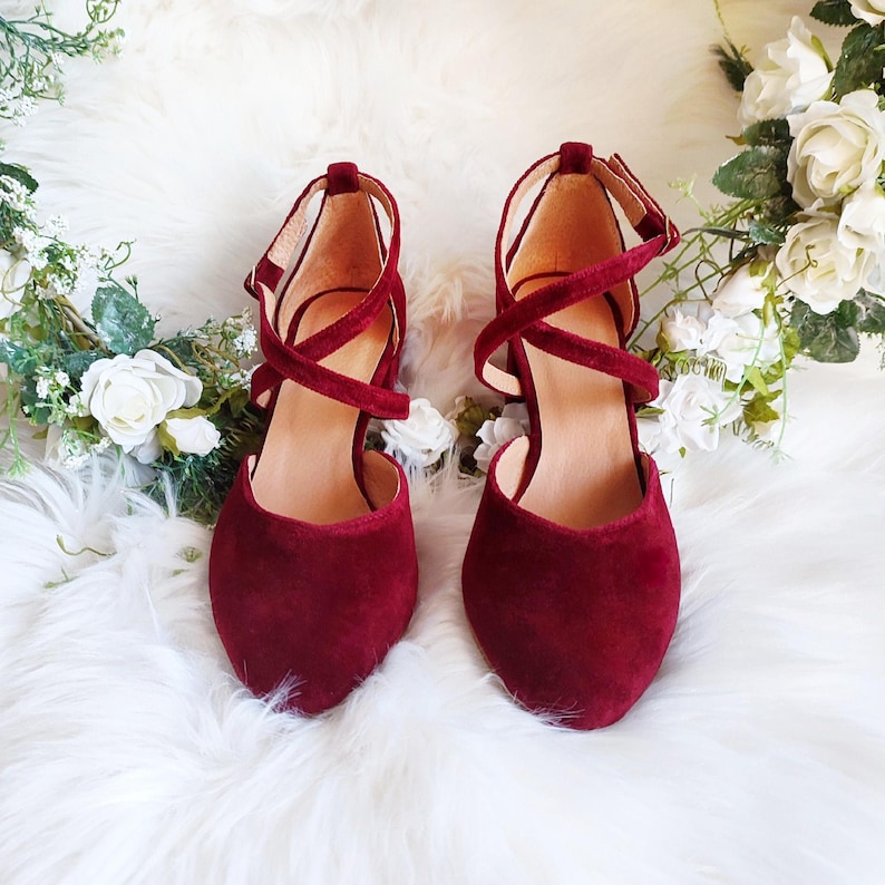 May include: A pair of burgundy suede heeled shoes with criss-cross straps.