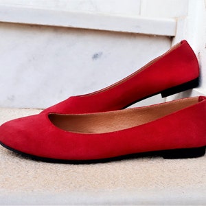 May include: A pair of red suede ballet flats with a black sole.