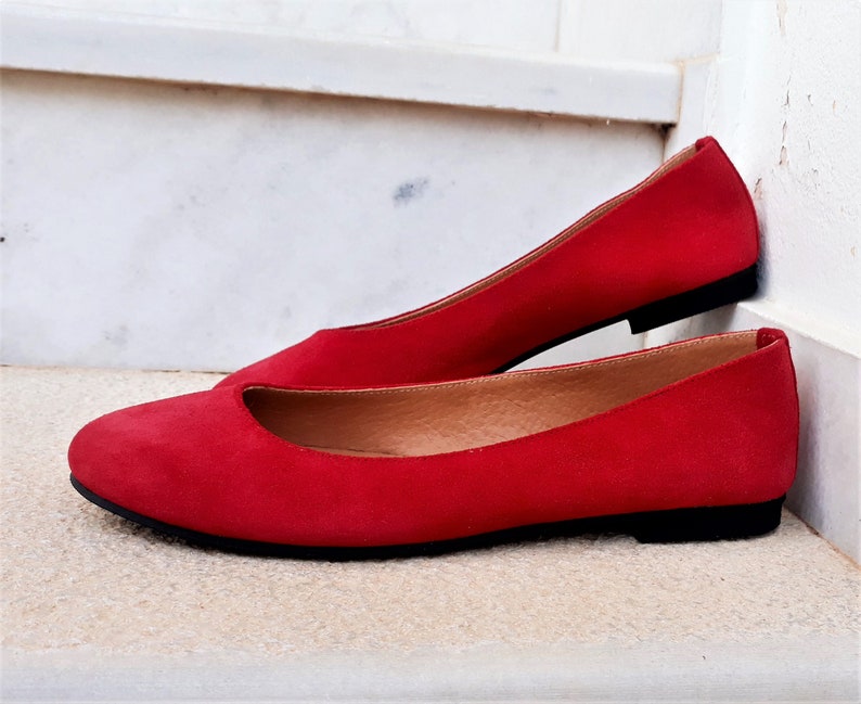 May include: A pair of red suede ballet flats with a black sole.