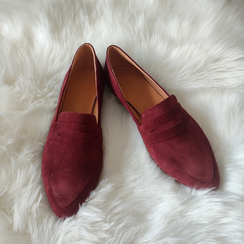 May include: A pair of burgundy suede loafers with a pointed toe and a single strap across the vamp.
