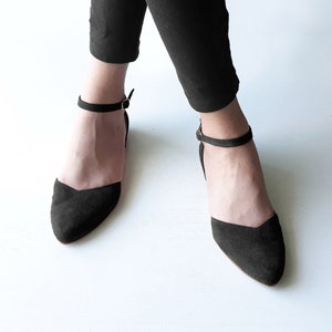 May include: A pair of black suede ankle strap flats with a pointed toe.