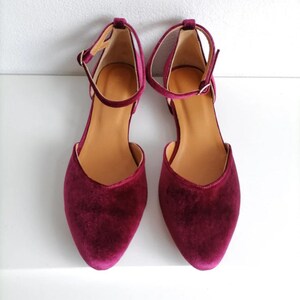 May include: A pair of burgundy velvet ankle strap flats with a pointed toe.