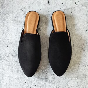 K&ouml;nnte beinhalten: Ein Paar schwarze Wildlederslipper mit Absatz und spitzer Zehenpartie. Die Slipper haben eine braune Ledersohle.