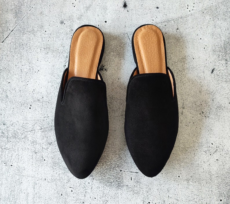 K&ouml;nnte beinhalten: Ein Paar schwarze Wildlederslipper mit Absatz und spitzer Zehenpartie. Die Slipper haben eine braune Ledersohle.