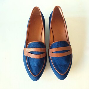 May include: A pair of blue denim loafers with brown leather accents. The loafers have a pointed toe and a slip-on design.